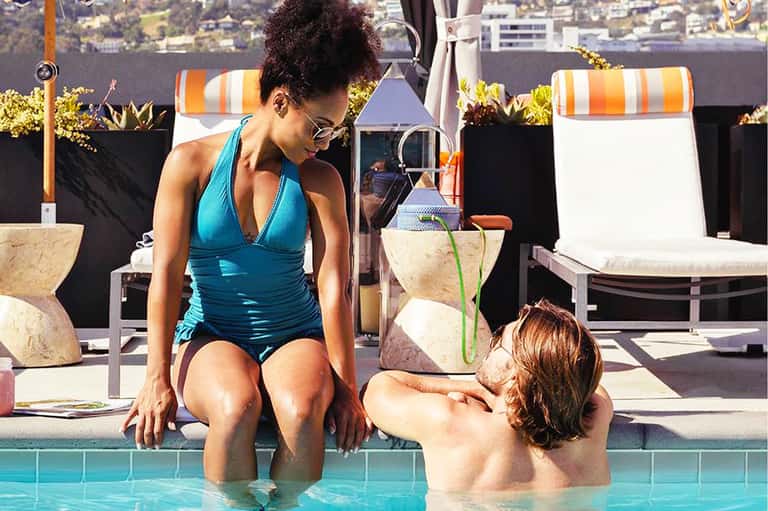Woman in turquoise swimsuit sitting poolside with child in water at upscale resort
