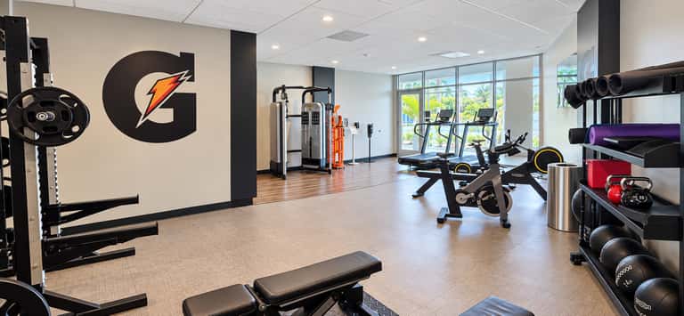 Modern gym with Gatorade logo, cardio equipment, weight racks, and large windows with natural light