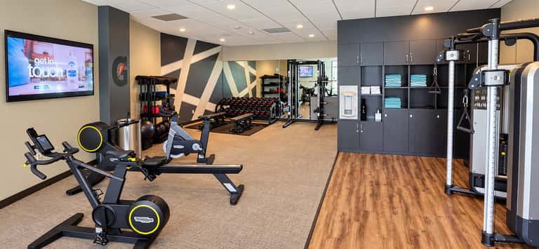 Fitness center with stationary bikes, dumbbells, strength equipment, TV screen, and organized storage