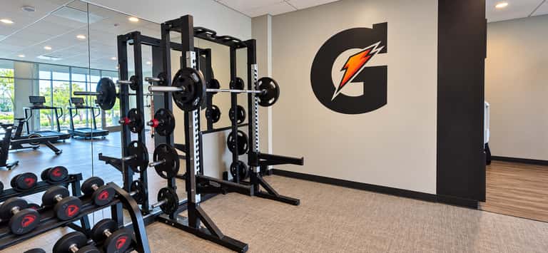 Weight training area with squat racks, barbell plates, and Gatorade branded wall in bright gym space