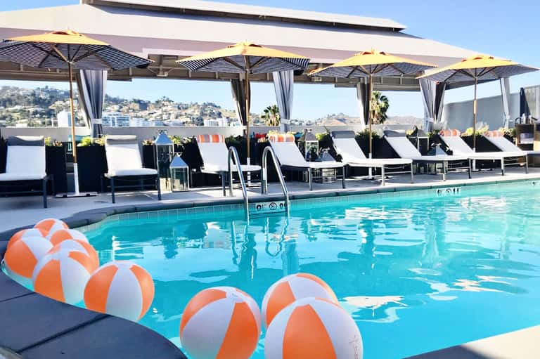 Resort pool with yellow umbrellas, lounge chairs, and hillside views with striped cabanas