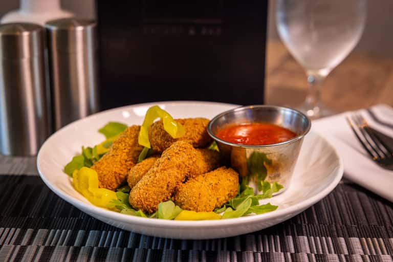 Golden fried kibbeh croquettes on bed of greens with red dipping sauce in small bowl