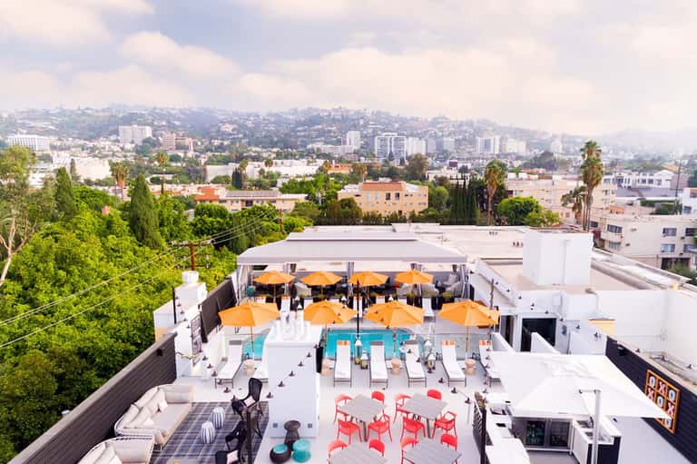 Urban rooftop pool deck with orange umbrellas, lounge chairs, and city skyline view