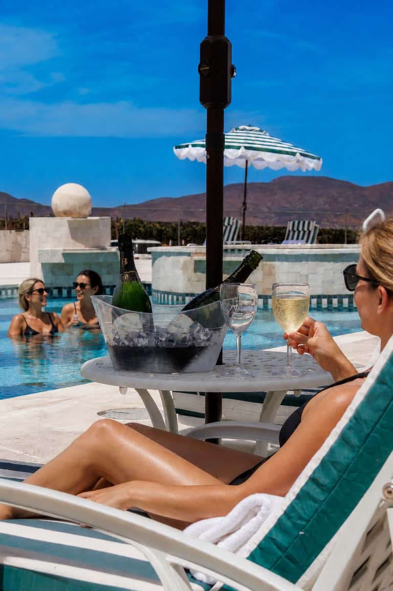 Woman enjoying champagne by luxury pool with mountain views and umbrella overhead