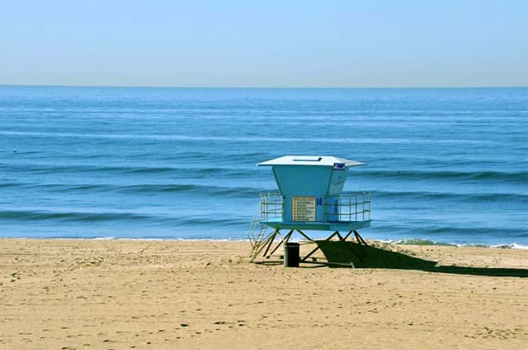 Turquoise lifeguard tower on sandy beach with calm blue ocean and clear sky