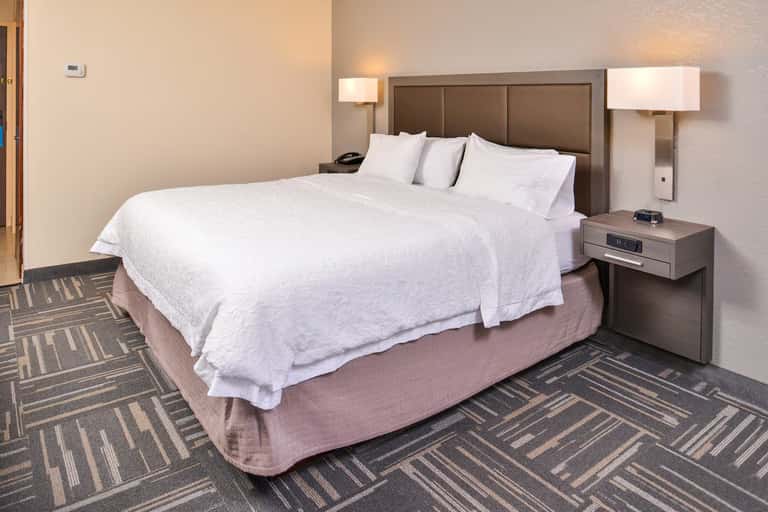 Single queen bed with white bedding in a hotel room with brown headboard and geometric patterned carpet