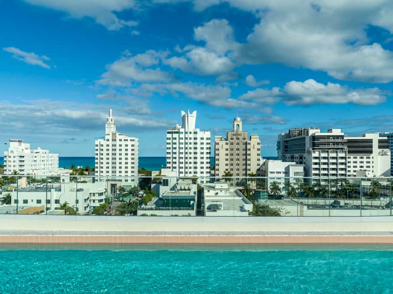 Beachfront Miami hotel skyline with Art Deco buildings, turquoise ocean, and white sandy beach under blue sky