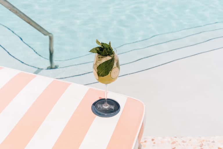 Mojito cocktail with mint and lime on striped beach lounger overlooking swimming pool