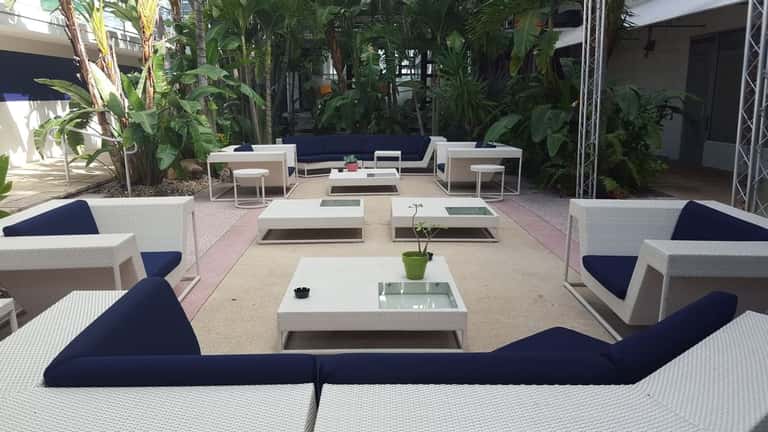 Modern outdoor lounge area with white wicker furniture, dark blue cushions, and lush tropical plants surrounding seating sections