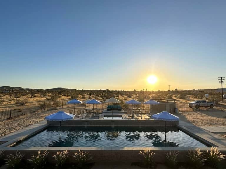 Rectangular pool with blue umbrellas and lounge chairs overlooking desert landscape at golden hour