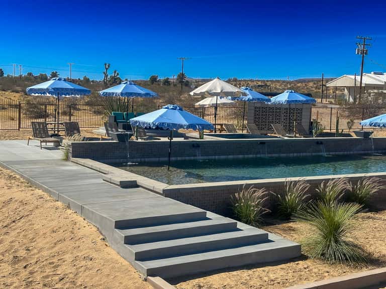 Natural hot spring pool with blue umbrellas, lounge chairs, and concrete deck in desert landscape