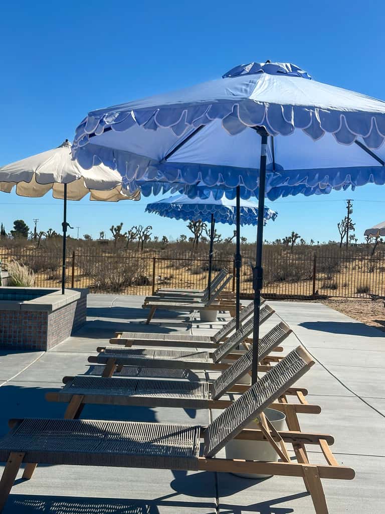 Blue and white striped umbrella over lounge chairs with desert hills and fence background