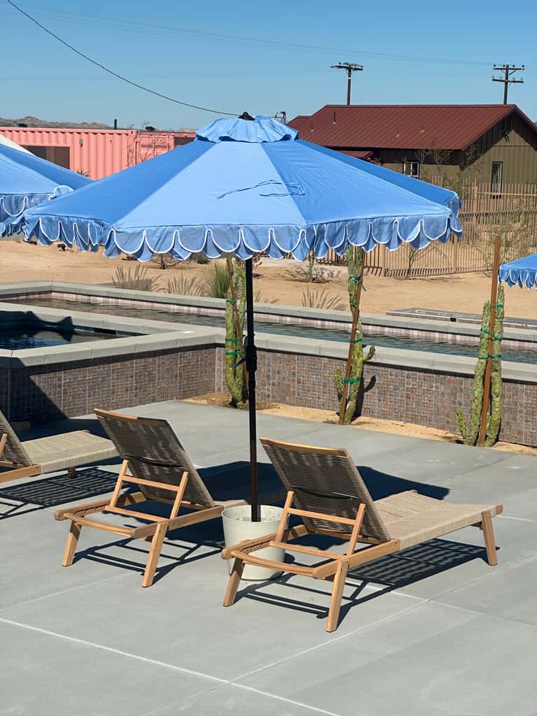 Single blue umbrella over two wooden lounge chairs beside a brick-lined pool