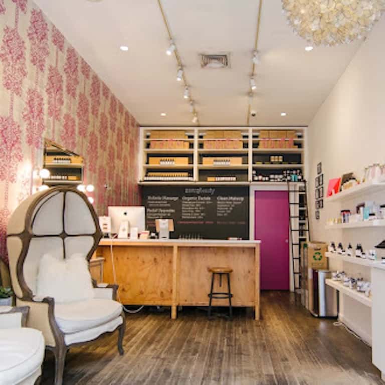 Upscale spa reception area with pink damask wallpaper, wooden counter, decorative chair, shelving, and hanging dried flowers