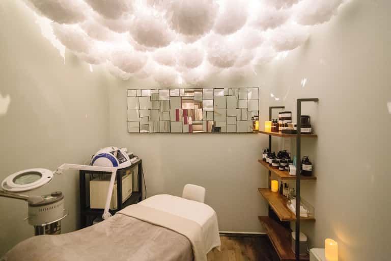 Professional spa treatment room with massage bed, shelving with products, and ambient lighting