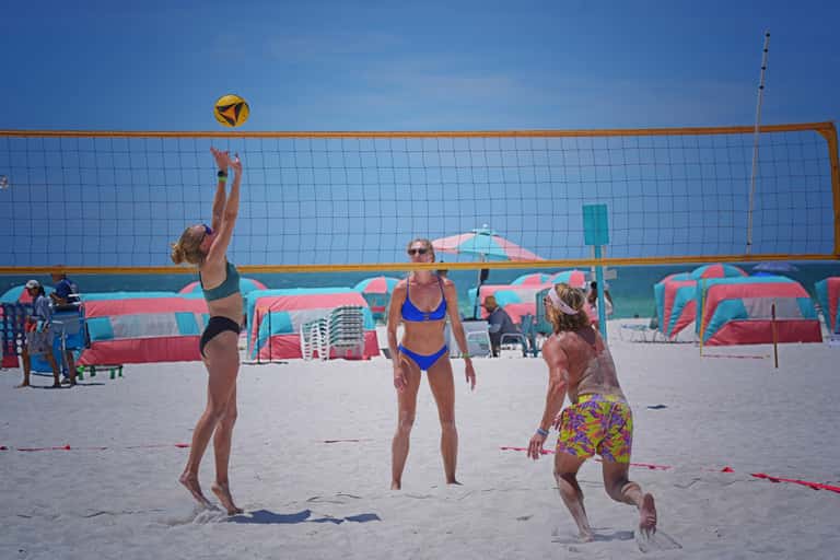 Beach volleyball players in action with pink and turquoise umbrellas in background