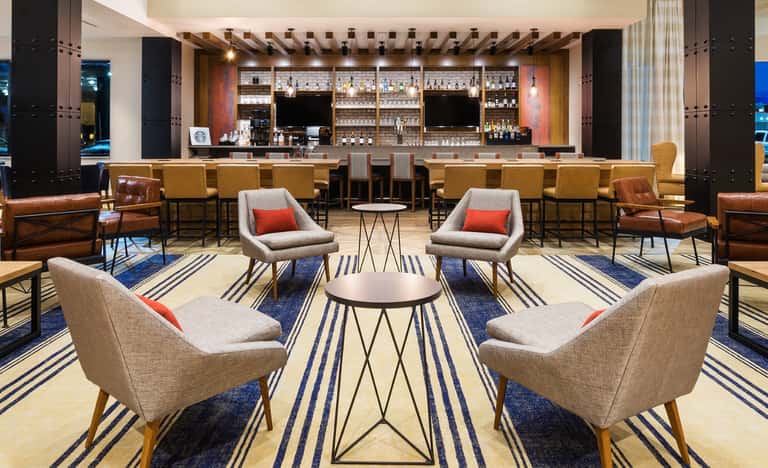 Contemporary hotel lounge with full bar, upholstered seating, geometric rugs, and warm ambient lighting