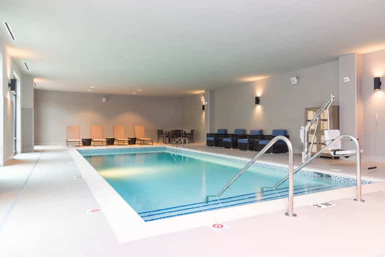 Indoor lap pool with lane markers, handrails, lounge chairs, and modern architectural design