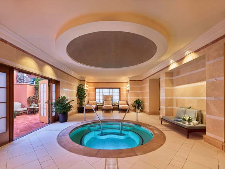 Luxurious indoor spa with circular hot tub, beige marble walls, skylights, and access to terrace seating