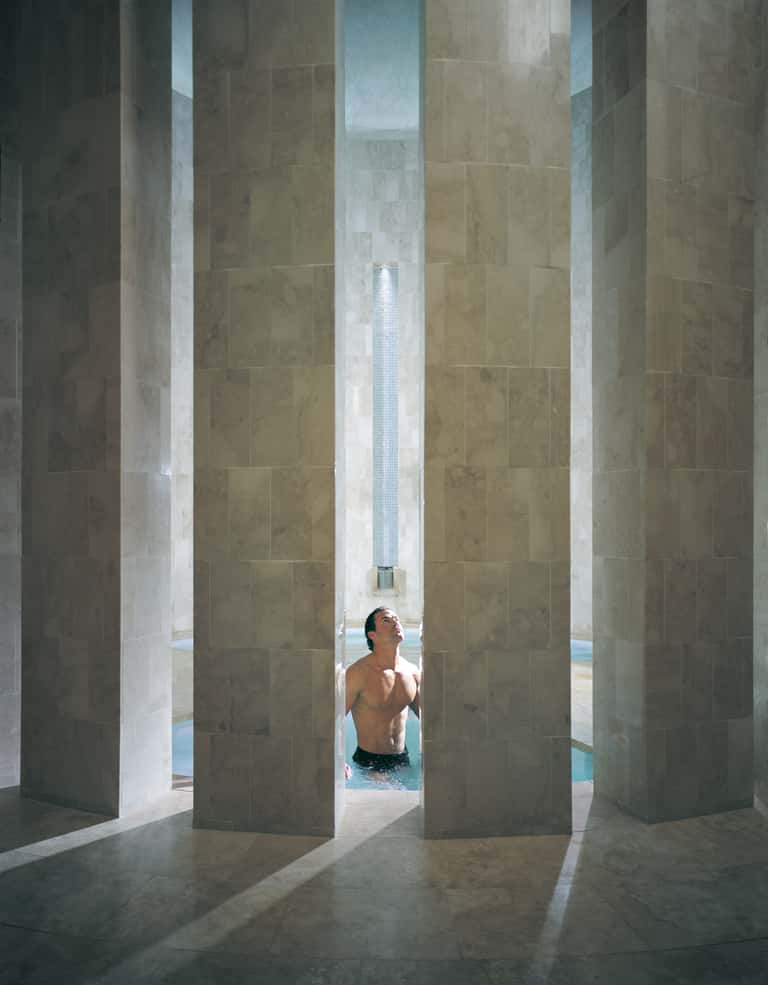 Man in swimming pool viewed through modern archways with green stone tile walls and natural light
