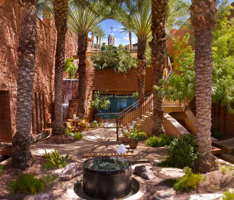 Spa courtyard with hot spring pool surrounded by red stone architecture, palm trees, and mountain views
