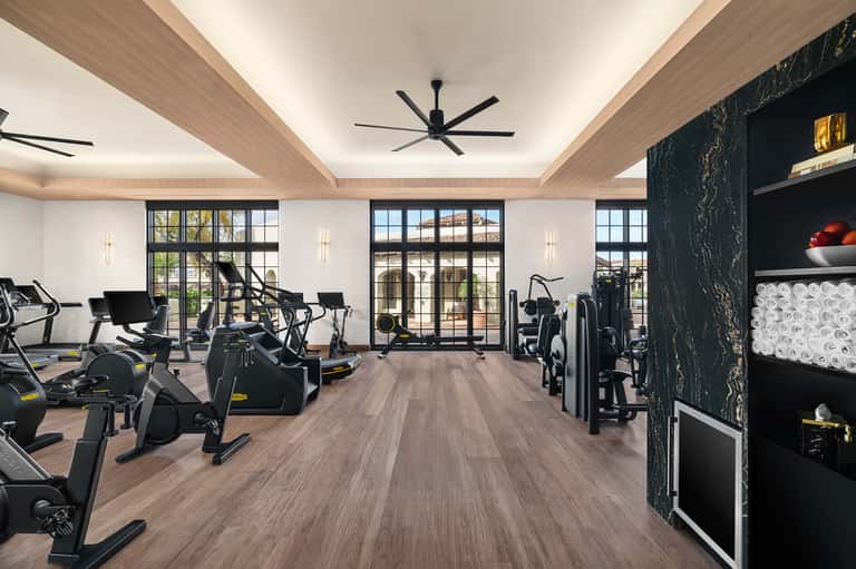 Modern gym with stationary bikes, cardio equipment, dark marble accent wall with towel storage, and expansive windows