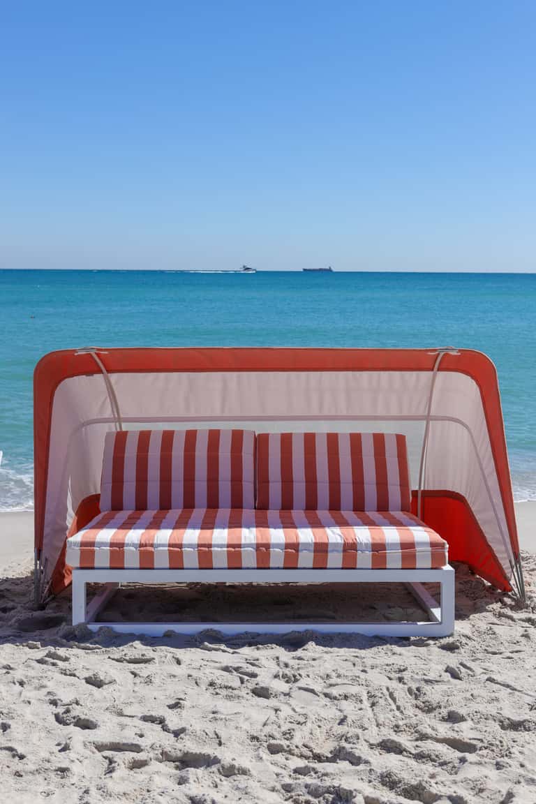 Red and white striped beach tent with cushioned seating on sand with ocean view