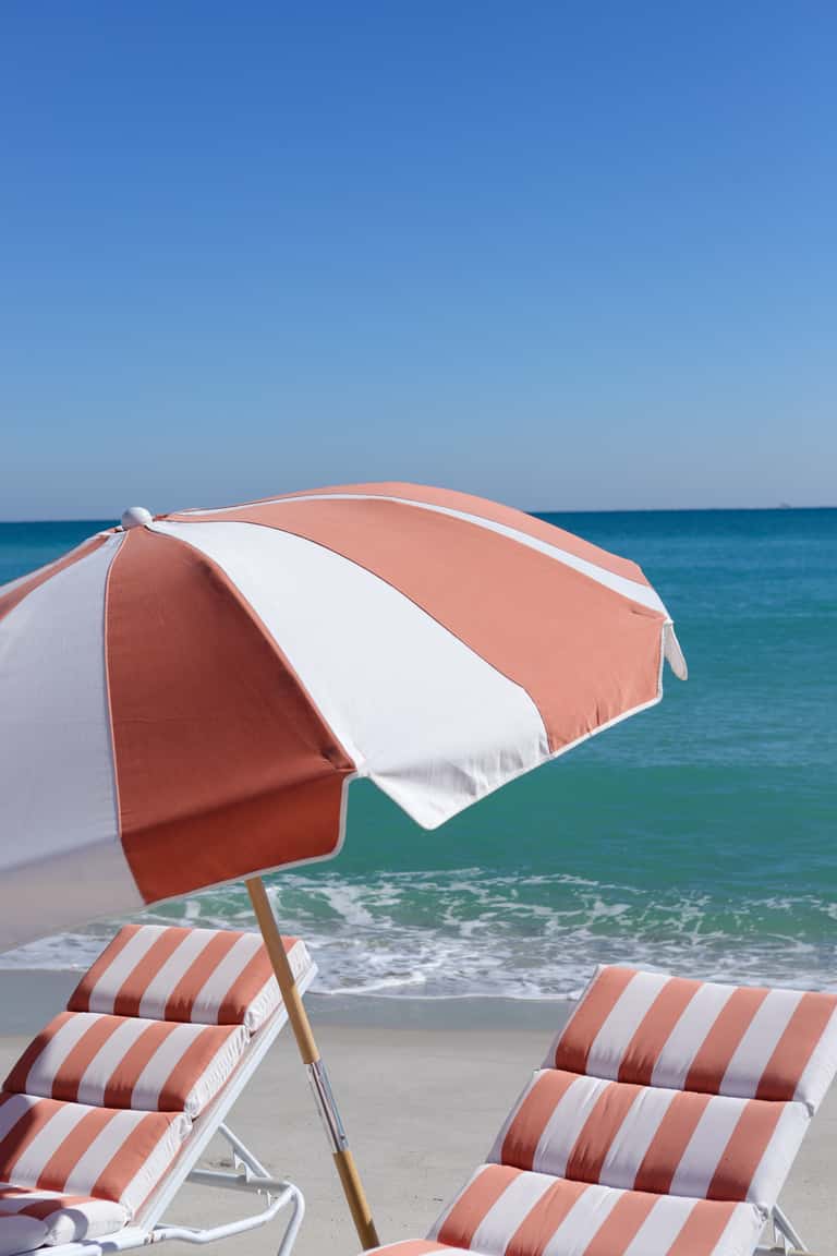 Red and white striped beach umbrella with matching loungers overlooking turquoise ocean waves