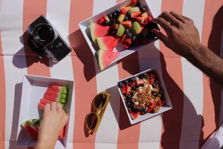 Overhead view of fresh fruit, camera, and breakfast items on red and white striped towel