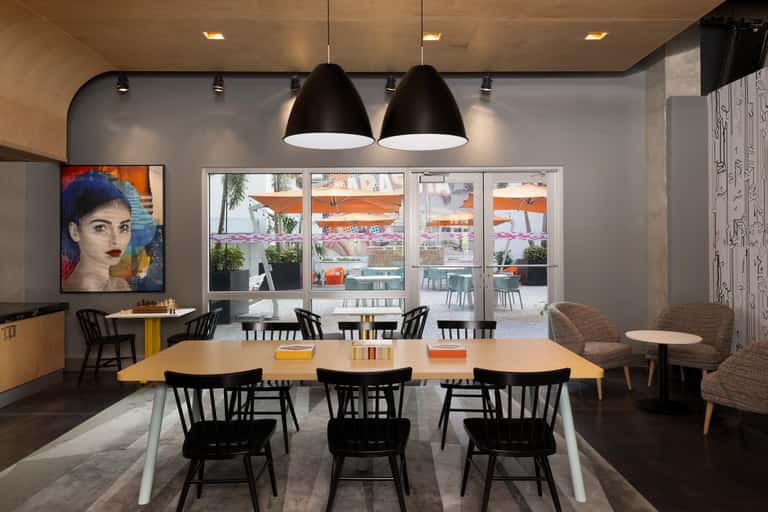 Modern dining area with large windows, wooden table, black pendant lights, and colorful artwork overlooking outdoor terrace