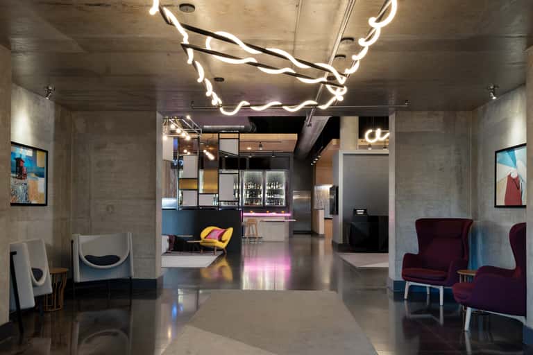 Urban hotel corridor with concrete walls, neon branch lighting, bar area, and modern furnishings