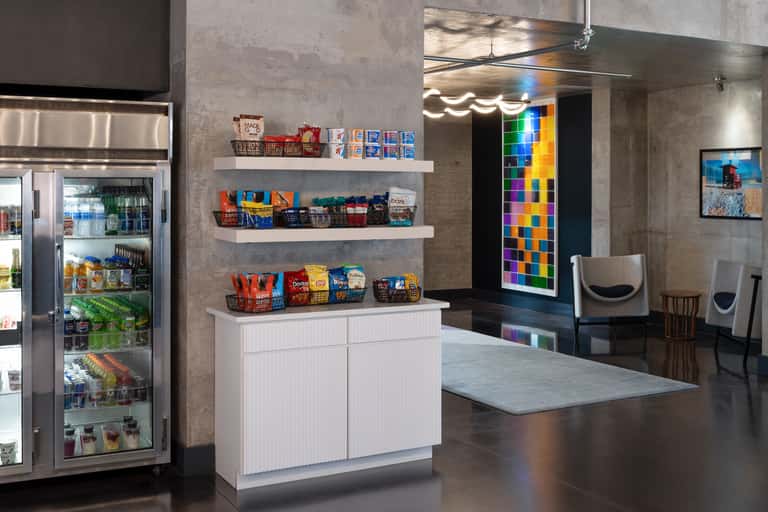 Modern hotel lobby with refrigerated market display, colorful digital art installation, and concrete finishes