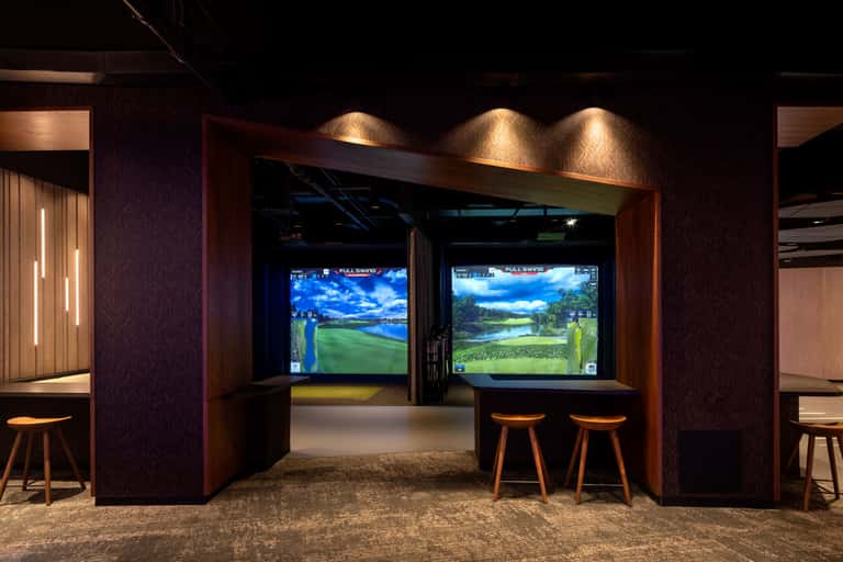 Indoor golf simulation room with two full-swing simulator bays and wooden framing with accent lighting