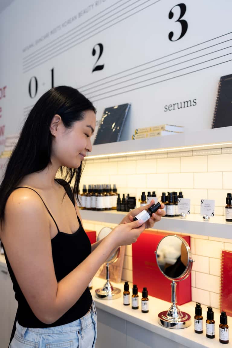 Woman examining serum product in modern spa retail display with numbered sections