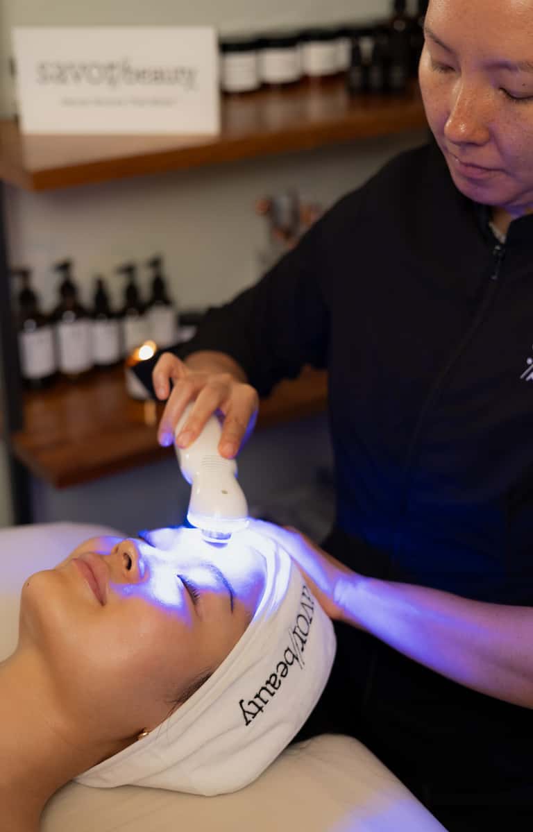Spa professional using LED light therapy device on client's face