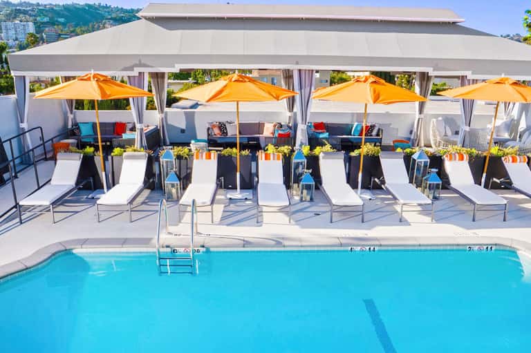 Resort pool deck with lounge chairs, orange umbrellas, white cabanas, and mountain views