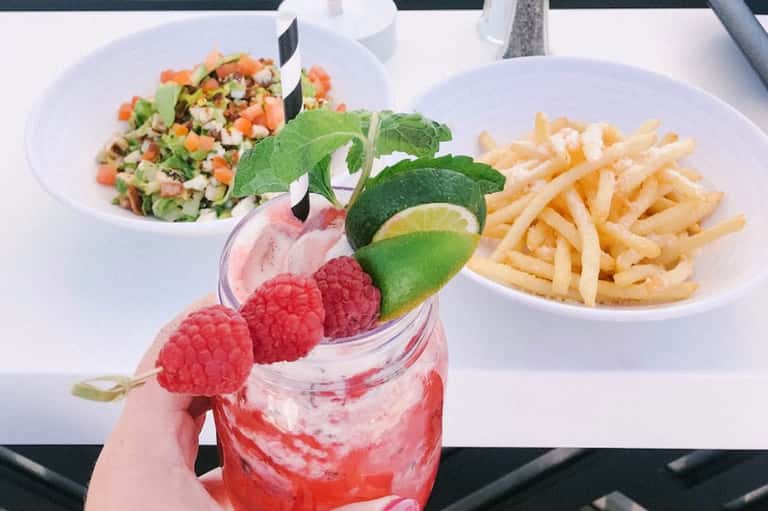 Gourmet meal featuring fresh salad, French fries, and raspberry-garnished cocktail served on white plates