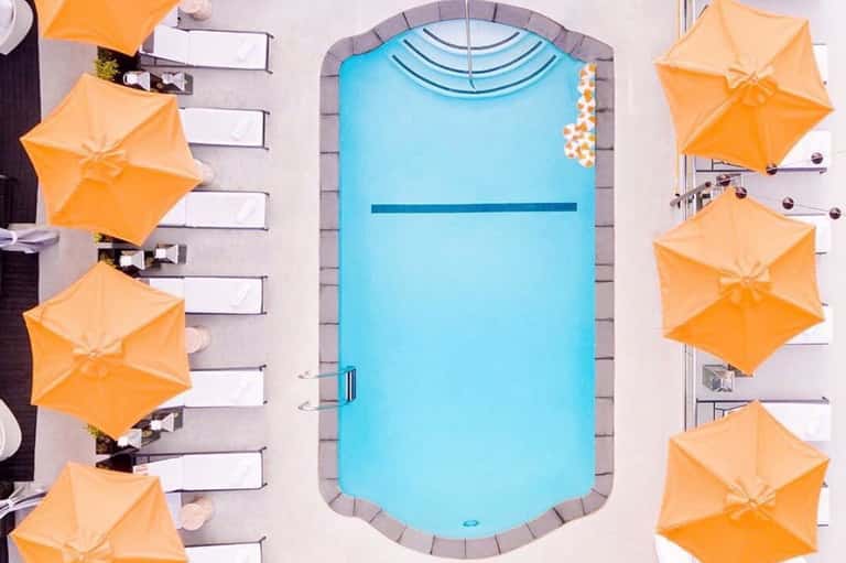 Overhead view of bright blue resort pool surrounded by orange umbrellas and lounge chairs