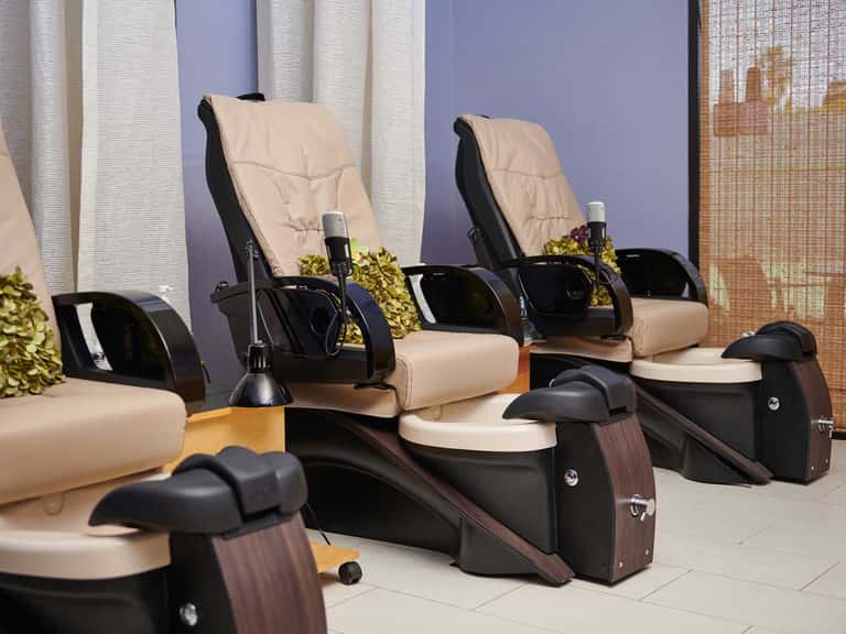 Pedicure station with cream and black massage chairs lined up in spa setting with purple walls