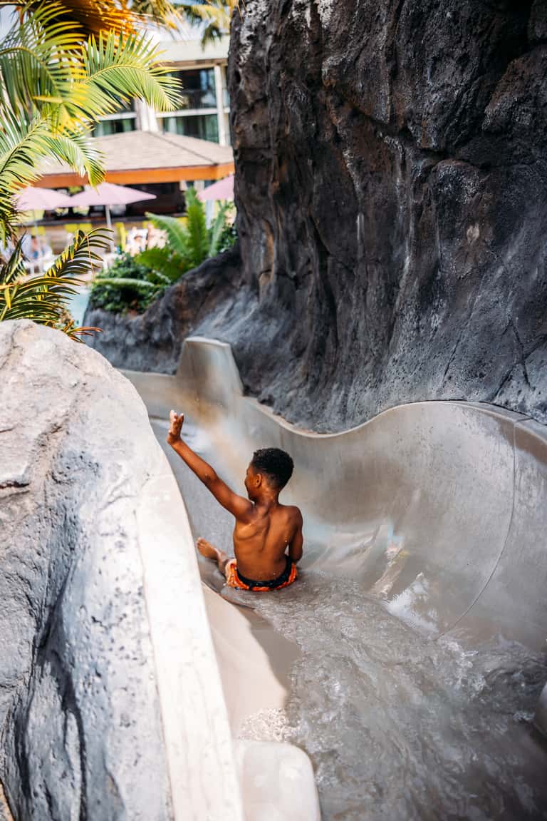 Young boy playing in a curved white water slide between rocky cliffs at a resort