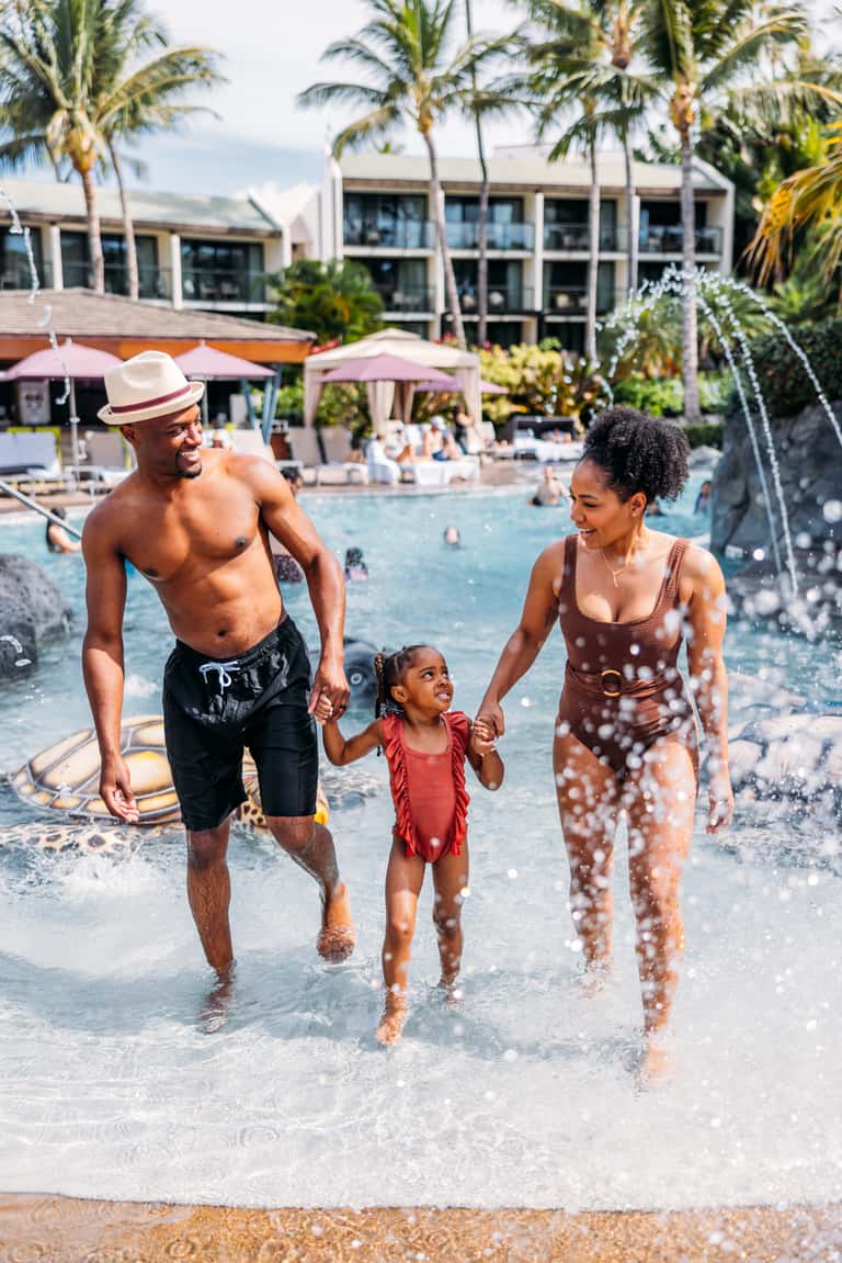 Family of three wading into calm ocean waters at a tropical beachfront resort