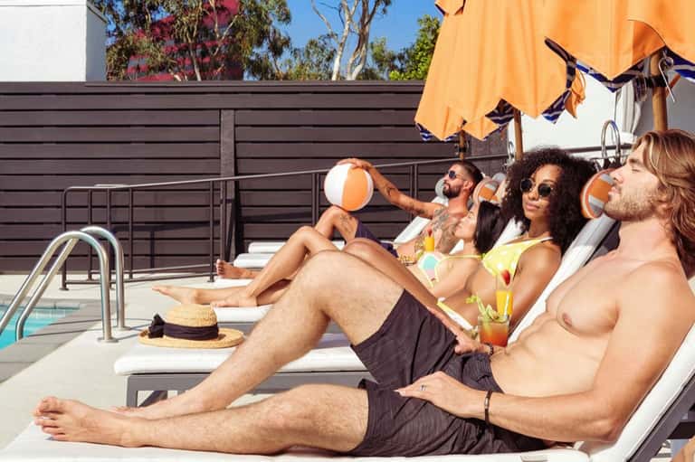 Group of guests relaxing on lounge chairs by a pool under an orange umbrella on a sunny day
