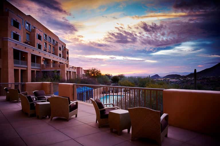 Desert resort terrace at dusk with lounge chairs, mountain views, sunset sky, and modern architecture