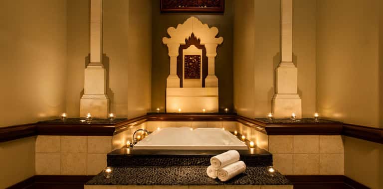Luxurious spa bath with carved golden shrine backdrop and candle-lit stone surrounds