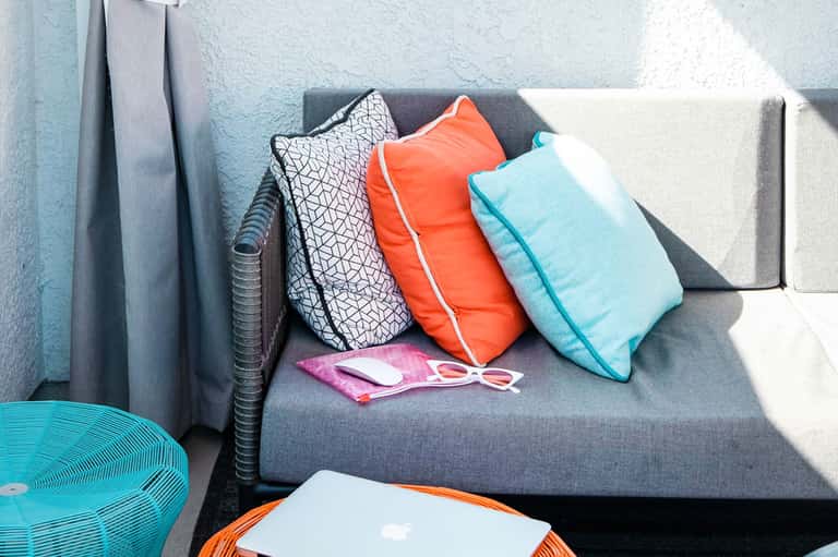 Colorful throw pillows in orange, turquoise, and patterned designs on a gray outdoor lounge chair