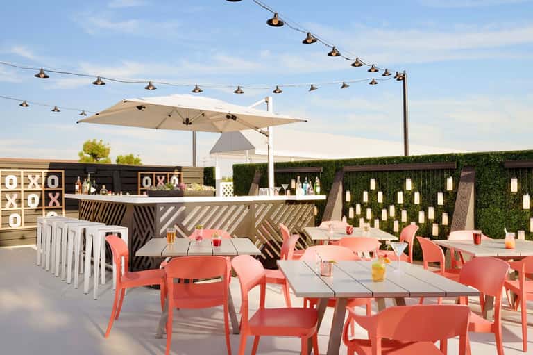 Upscale rooftop bar and dining area with coral-pink chairs, white bar counter, and large umbrella