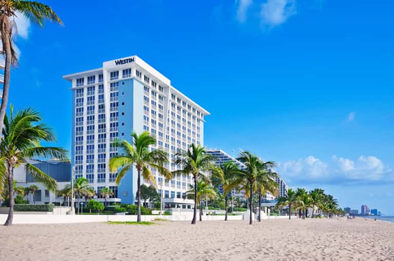 Beachfront hotel with white Westin building and palm trees on sandy shore
