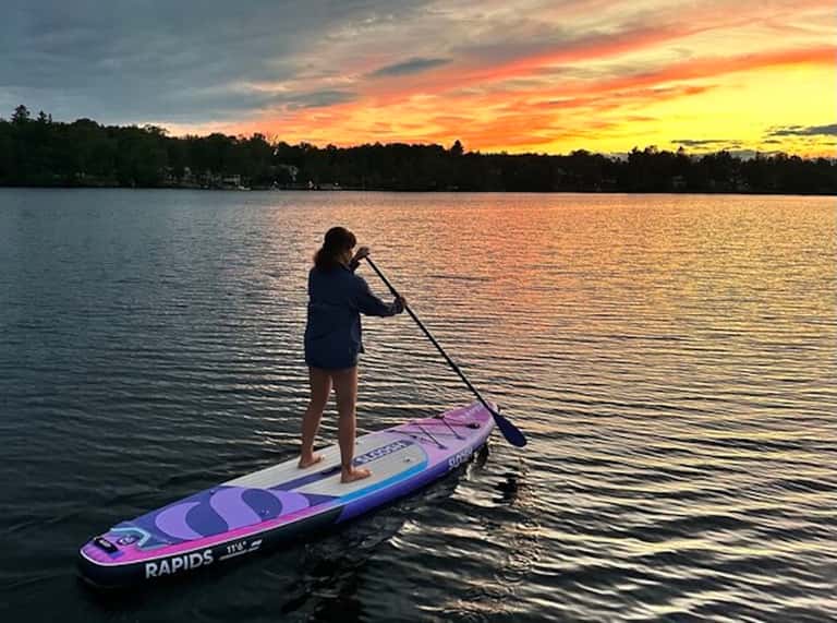 Woman stand-up paddleboarding on lake at sunset with colorful board