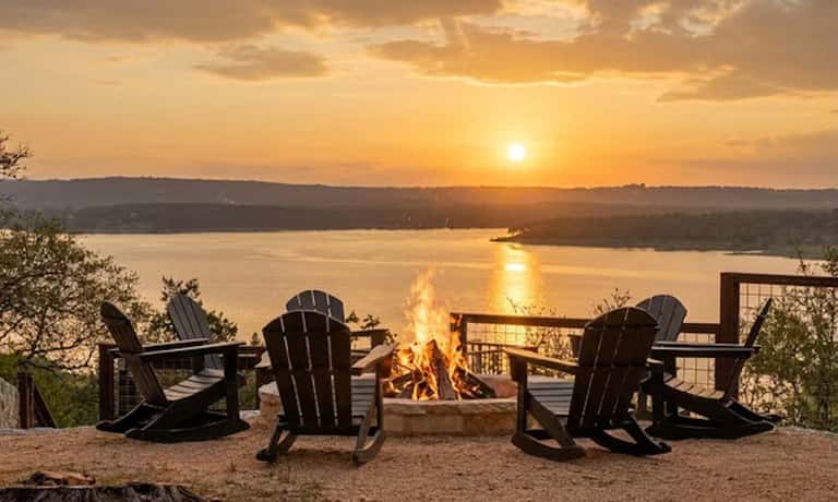 Fire pit with Adirondack chairs overlooking lake at golden sunset