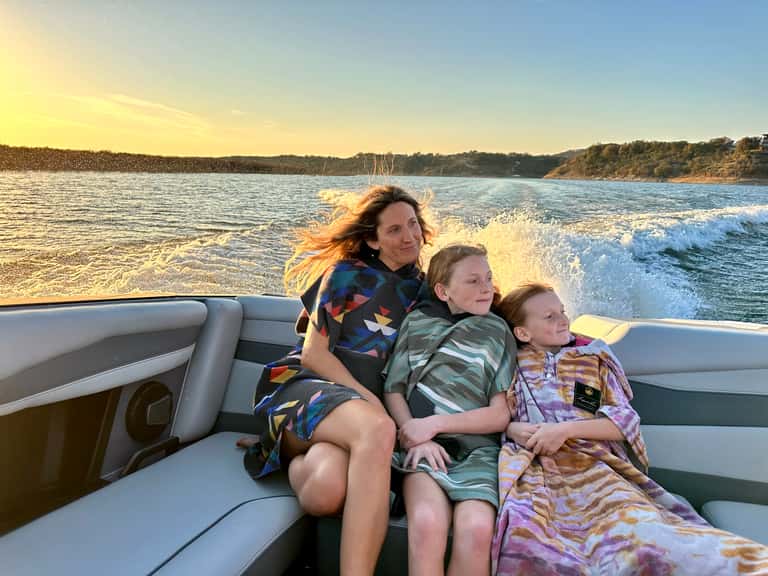 Woman and two children enjoying a speedboat ride on calm blue water at golden hour with scenic coastline background